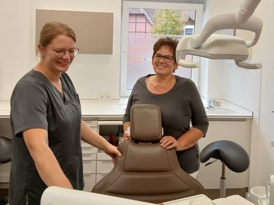 Zwei Mitarbeiterinnen stehen lachend am braunen Behandlungsstuhl